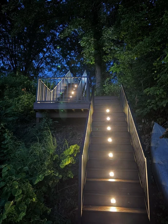 Illuminated composite staircase leading through a wooded lakeside property